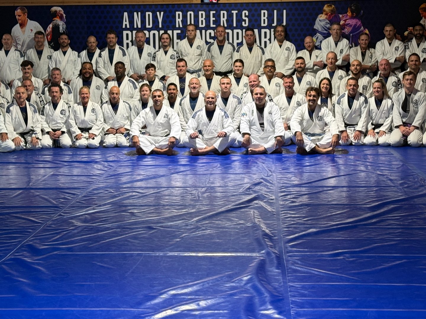 Royce Gracie seated in the front row with black belts and students of the Royce Gracie network on the mats at Andy Roberts BJJ